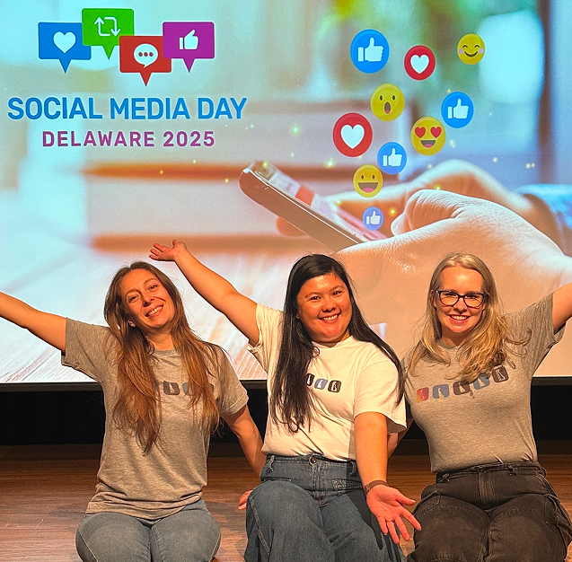 ECF Social Media Day DE Photo of three smiling women on a stage in front of a screen displaying “Social Media Day Delaware 2025” and social media icons. Three ECF team members smiling on stage at the Social Media Day Delaware conference in front of a screen displaying social media icons.